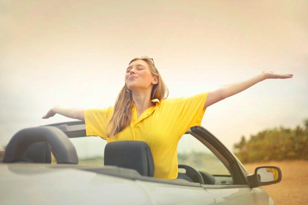 mujer blanca joven con los brazos al aire dentro y expresion de alegria despues de ahorrar para comprar un carro
