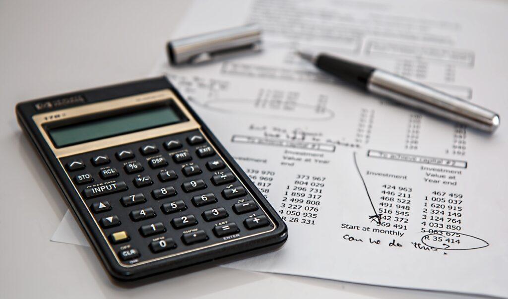 calculadora, papeles financieros de los tipos de inversiones y un bolígrafo sobre un fondo blanco